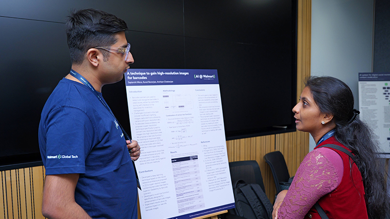 A Walmart Global Tech associate and an attendee having a discussion in front of a technical poster at AI @ Walmart. 