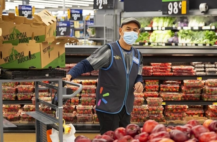 An employee wearing a mask and a vest with Walmart Spark half logo surrounded by fresh produce