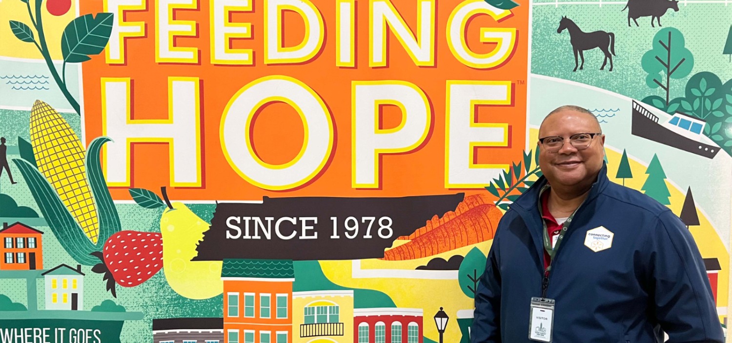 male associate standing in front of a colorful mural that reads "feeding hope since 1978"